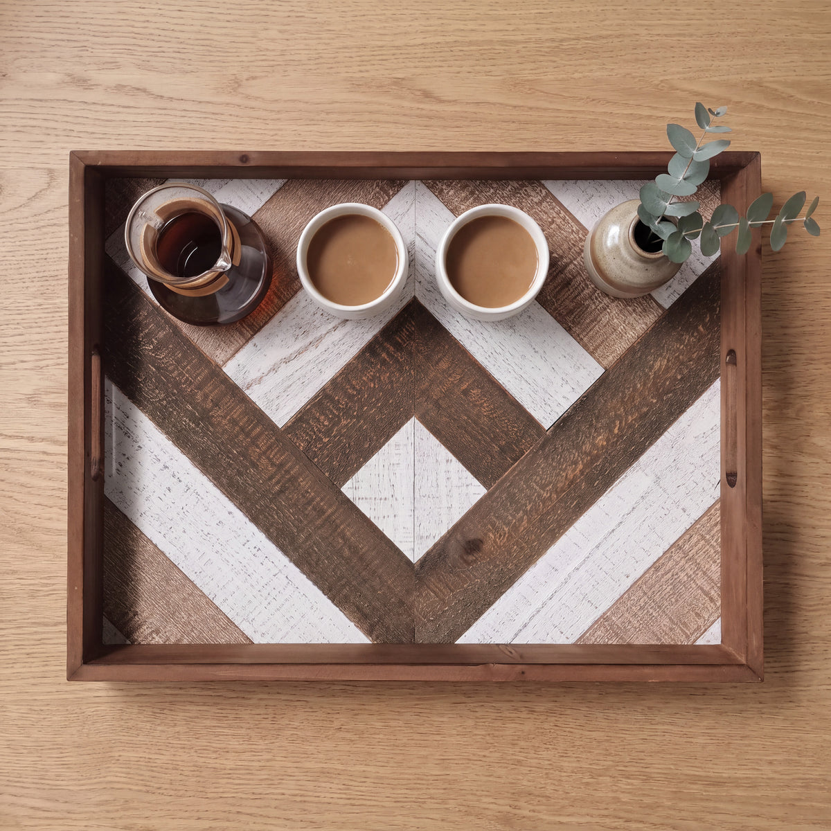 Houten dienblad met visgraatmotief op een eiken salontafel, met koffie en een vaasje eucalyptus