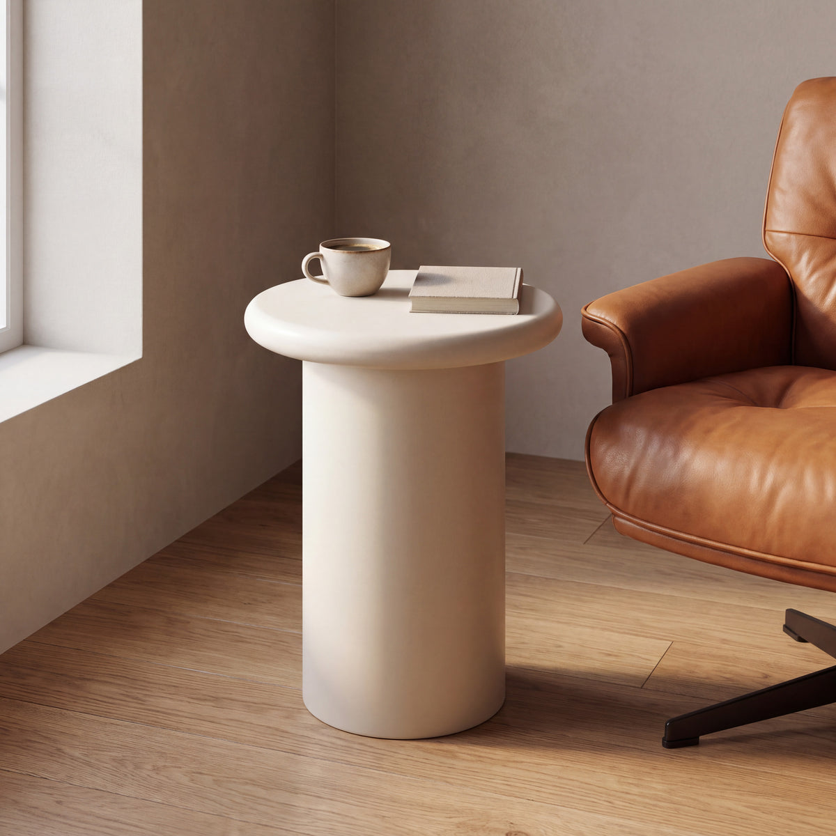 Liora paddenstoel-bijzettafel in mat crème naast een cognackleurige fauteuil, met koffie en een boek