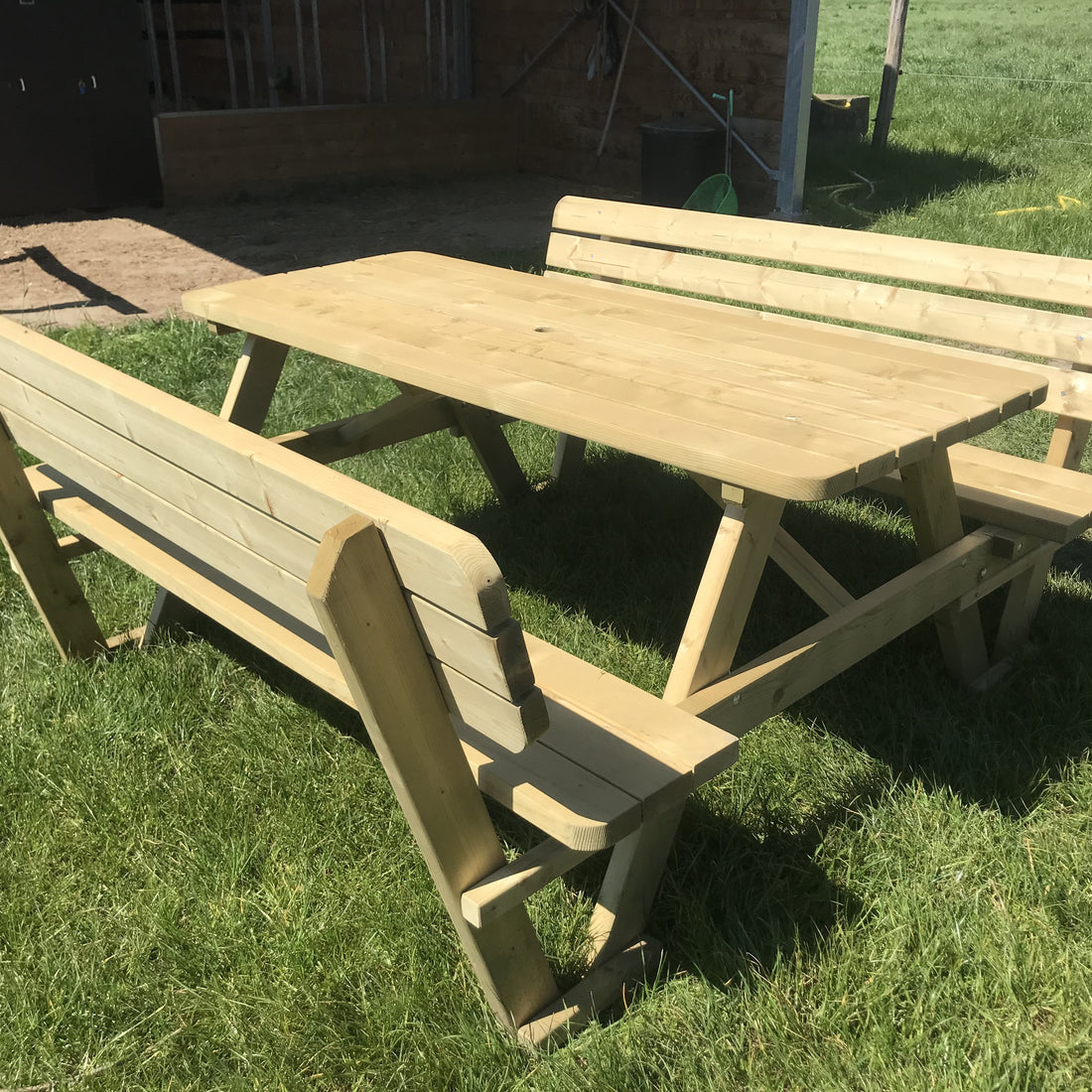 Picknicktafel 180 cm met rugleuningen op het gras, met een schuur op de achtergrond