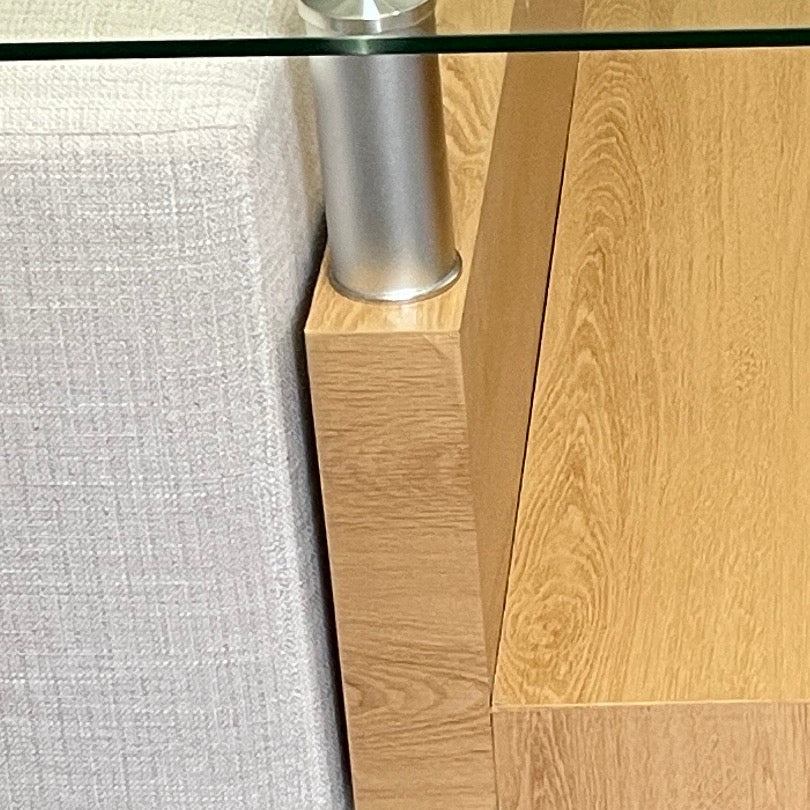 Close-up van het glasblad op een metalen steun, het onderstel met eikendecor en de stof van een poef