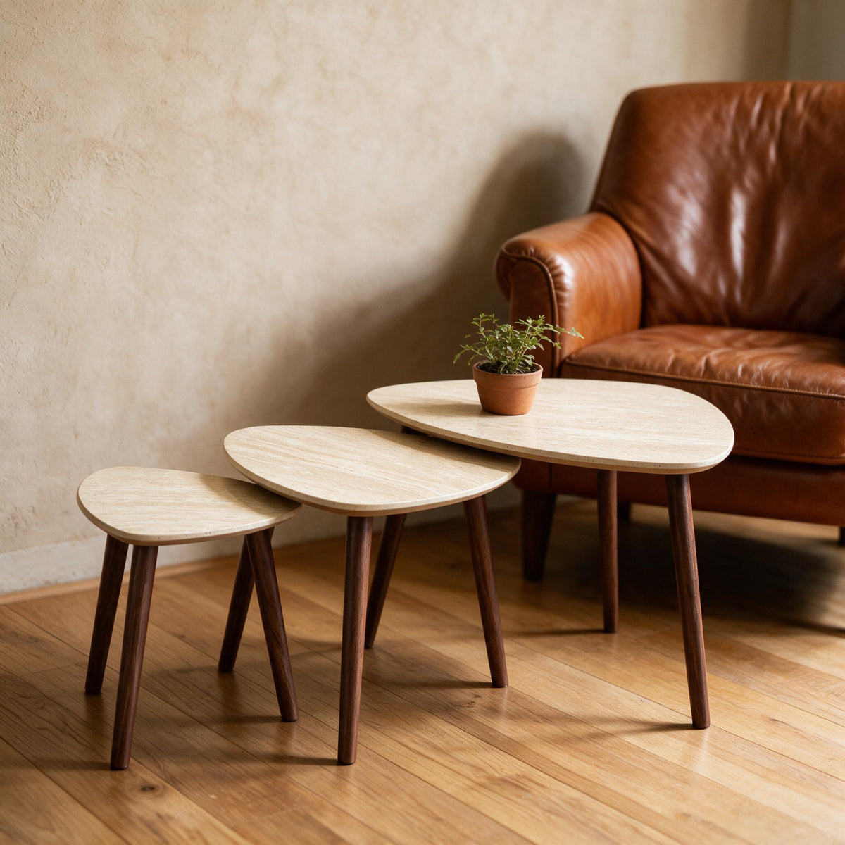 Set van drie driehoekige bijzettafels in travertijnlook naast een fauteuil, met plantje
