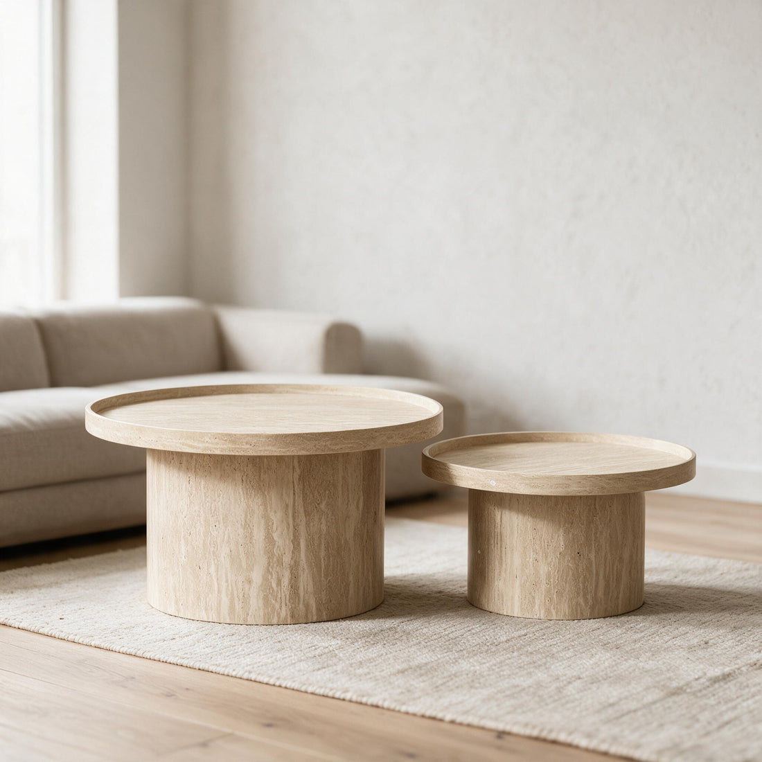 Set van twee ronde salontafels in travertijnlook met opstaande rand, in een lichte woonkamer